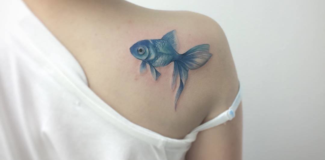 A tiny goldfish tattoo behind a girls ear is sweet symbol of good fortune  and prosperity  Ratta Tattoo